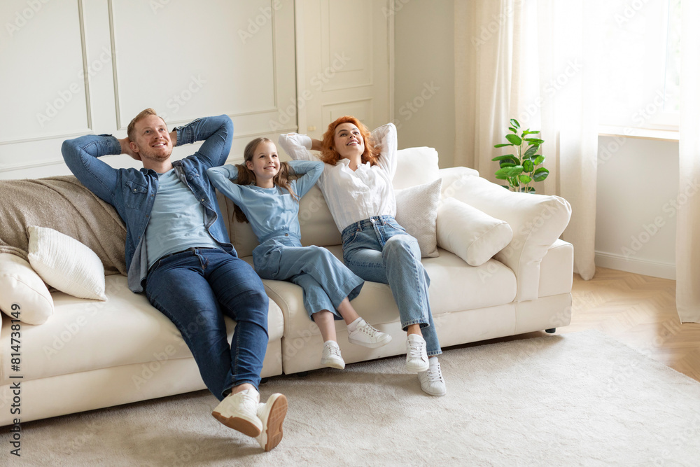 Relaxed parents and daughter resting on sofa with closed eyes and hands behind heads in living room interior, full length shot, free space Relaxed parents and daughter resting on sofa with closed eyes and hands behind heads in living room interior, full length shot, free space