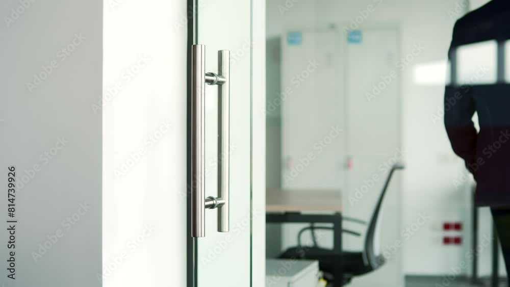 Close up of a man's hand opening a glass office door holding a metal doorknob in a modern building. A man, businessman or employee in a formal suit opens the door and enters the workplace inside