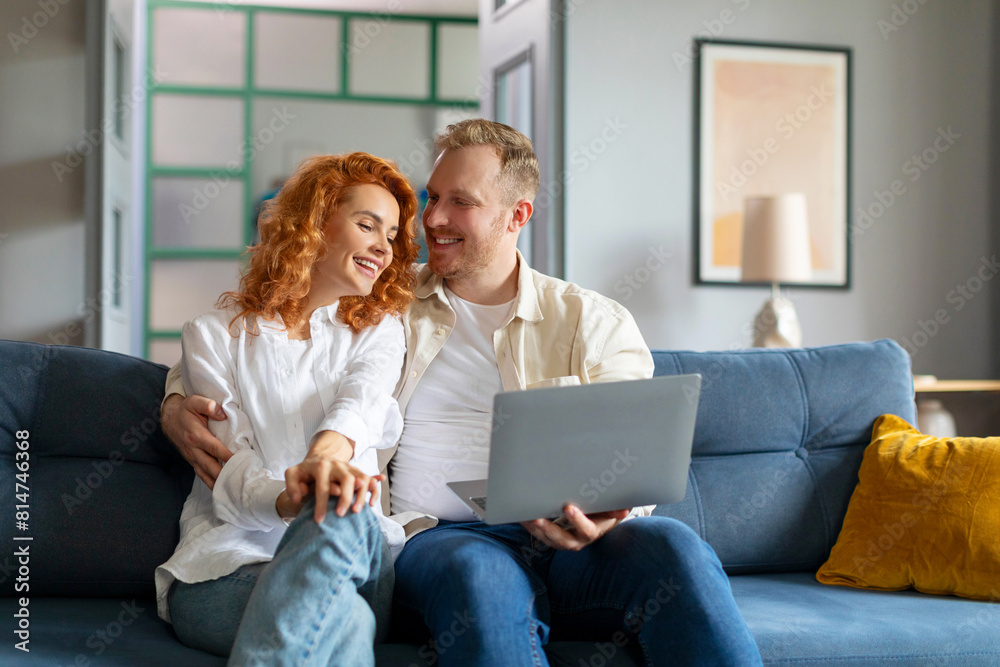 Happy European couple using laptop computer and embracing, relaxing on couch in living room, shopping together online, copy space Happy European couple using laptop computer and embracing, relaxing on couch in living room, shopping together online, copy space