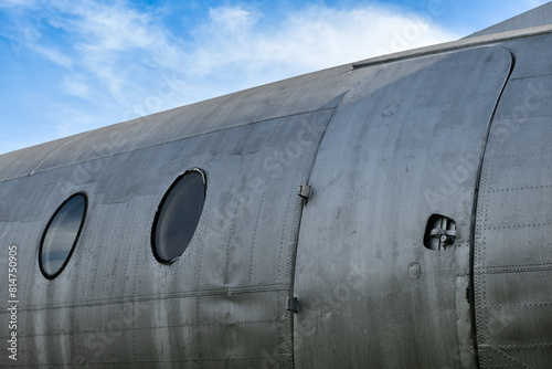 Emergency exit doors and windows of an old commercial airplane showing silver metal surfaces and parts on a blue sky background.