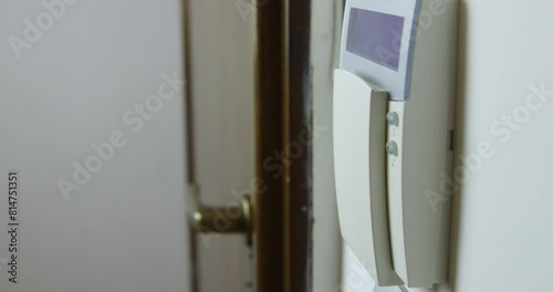 A mans hand is captured as he sets an alarm on a wall-mounted security keypad inside a house, ensuring safety and security.