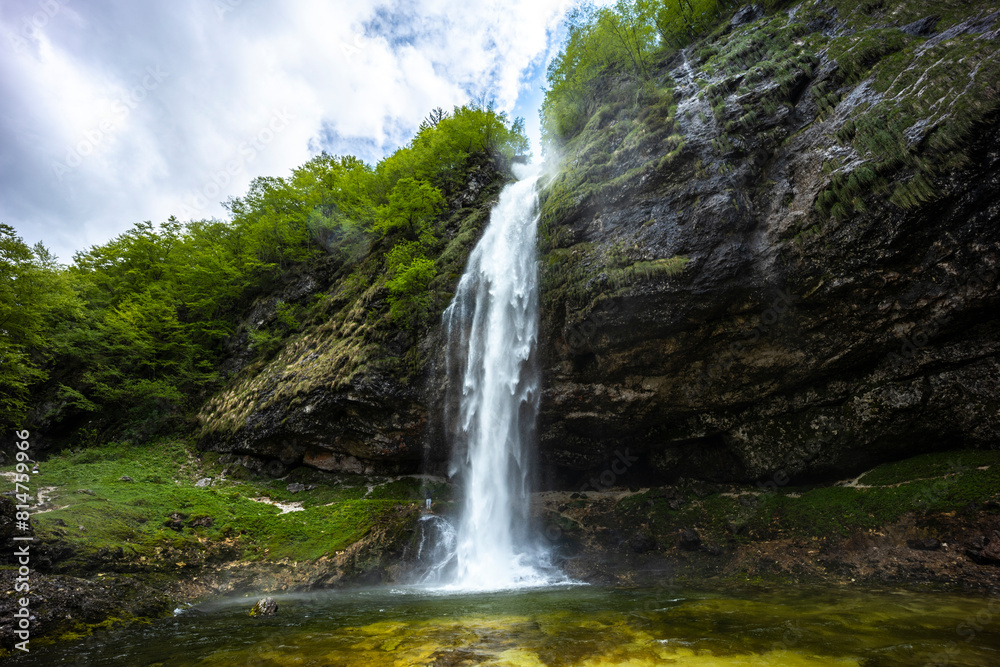 Fototapeta premium Fontanon of Goriuda, Udine. Wonderful waterfall that falls from a cliff. The force of the waterfall is a sight to behold. Hiking, trekking in the open area surrounded by woods. Summer holidays, peace.
