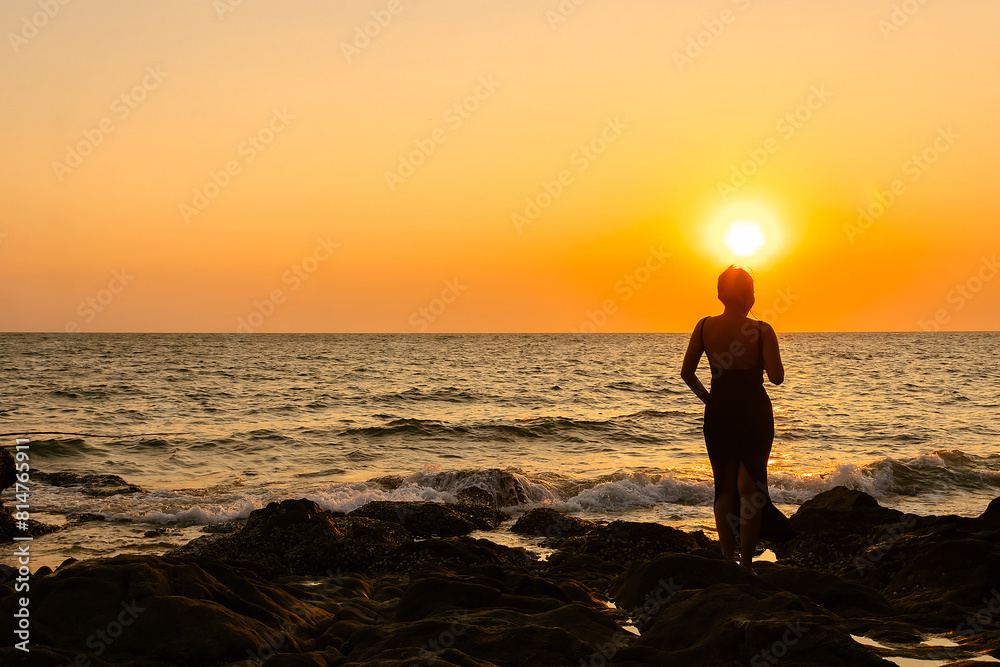 Happy Carefree Woman Standing on Rock and Watching Sunset. Beautiful Woman Silhouette at sunset.