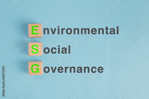 A wooden block on pastel blue paper background with the green letters ESG written on it. Concept of Environmental, social and governance principle for public responsibility.