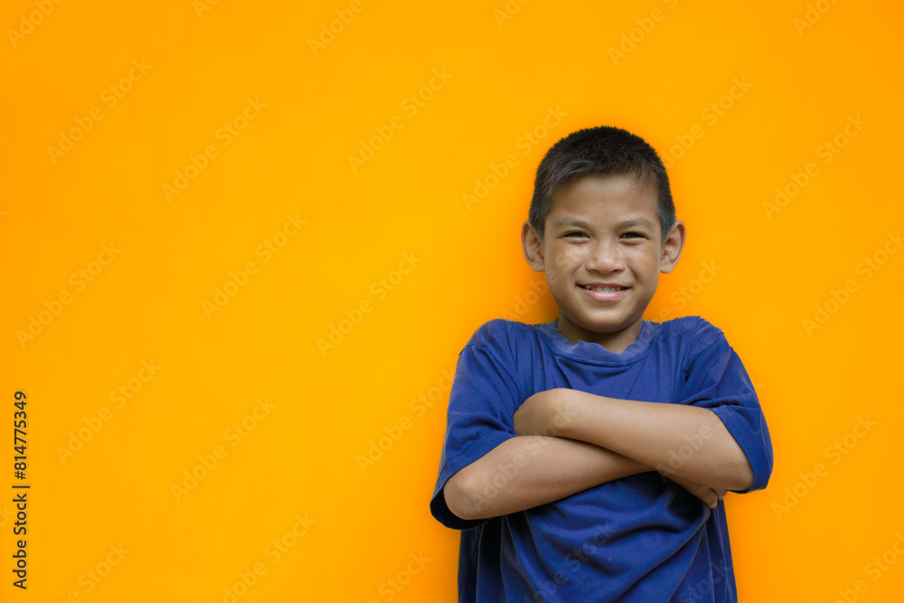 Cute boy smiling and is using both hands to fold his arms around his chest or cross one's arm are ready to fight in an isolated light yellow color studio background. Cute boy smiling and is using both hands to fold his arms around his chest or cross one's arm are ready to fight in an isolated light yellow color studio background.