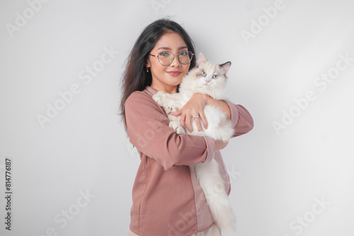 Canvastavla Lovely Asian woman wearing eyeglasses holding her ragdoll cat and smiling to the camera isolated over white background