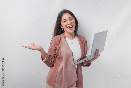 Excited young Asian business woman holding a laptop while pointing to the copy space beside her on isolated white background.