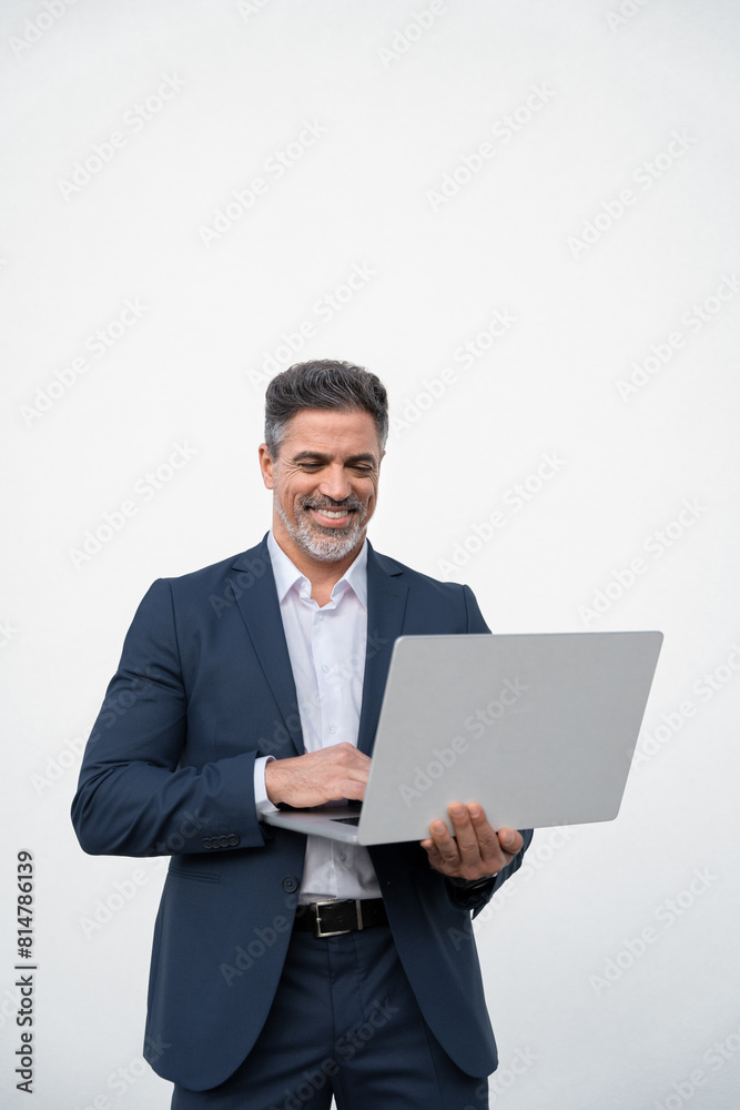 Vertical portrait of middle age mature businessman using pc laptop for business work. Smiling handsome latin older man in formal suit holding desktop computer. Isolated white background, copy space Vertical portrait of middle age mature businessman using pc laptop for business work. Smiling handsome latin older man in formal suit holding desktop computer. Isolated white background, copy space
