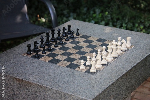Beautiful large granite chess table stands prepared with black and white playing pieces in the garden