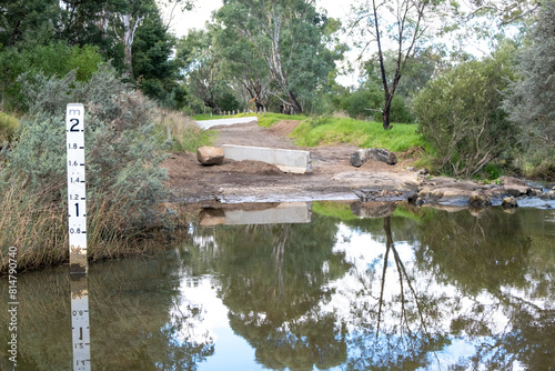 Fotografie A closed and flooded dirt road with a depth indicator or Flood Depth Marker Sign with increments up to 2 meters to show the water level at a river crossing in rural Australia