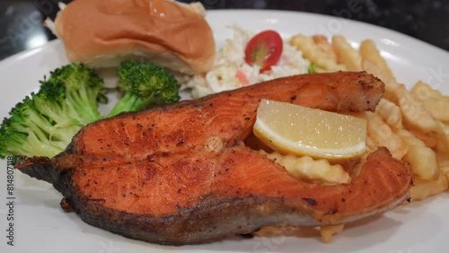 Grilled salmon fish steak with lemon slice, salad, broccoli, bread and French fries.