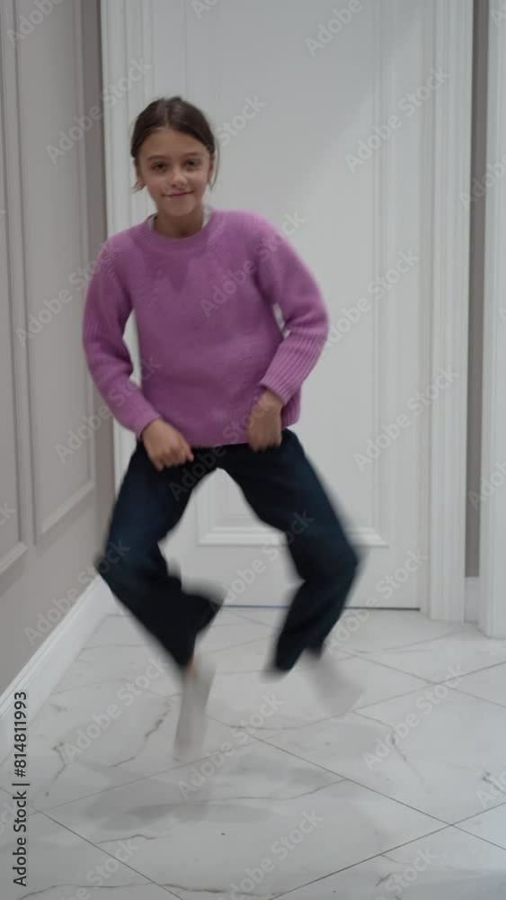 Cheerful young girl wearing pink sweater performs a dance routine in well-lit white hallway for social media challenge Cheerful young girl wearing pink sweater performs a dance routine in well-lit white hallway for social media challenge