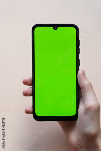 hands holding a phone with an empty green screen on a monochrome background. free space for text
