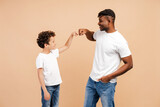 Happy African American man and little boy, father and son wearing white t shirts giving fist bump