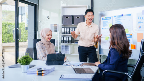 Comprehensive financial chart adorns the whiteboard during a presentation  where male and female business professionals  including a Muslim woman in hijab  engage in a productive meeting.