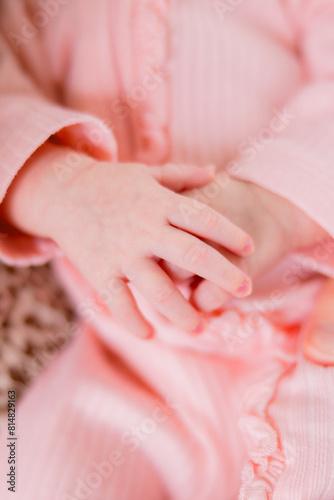A newborn baby girl has her hands together. She is dressed in an all pink feminine outfit.