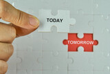 Hand holding piece of jigsaw puzzle with words Today and Tomorrow.