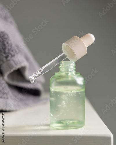 Droplet falls from a pipette set on a glass bottle filled with green liquid near folded towel
