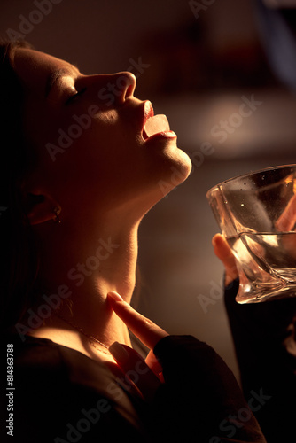 A beautiful girl erotically holds an ice cube with her lips.