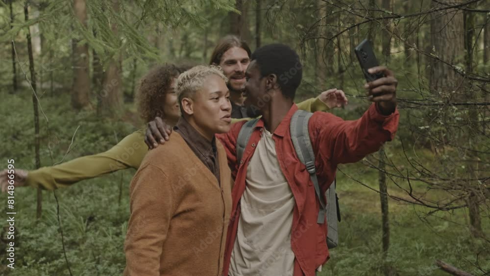 Group of joyous friends smiling and posing for smartphone camera while taking selfie together during summer hike in forest Group of joyous friends smiling and posing for smartphone camera while taking selfie together during summer hike in forest