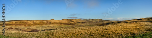 Panoramic view of a dry barren grassland prairie with small hills under a bright blue sky. 
