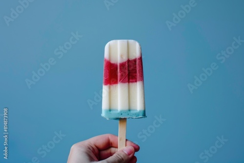 A hand holding a homemade popsicle with distinct layers of red, white, and blue against a clear blue sky background, offering a refreshing treat that echoes patriotic themes. photo