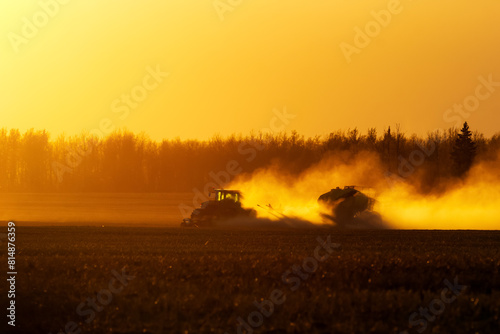 Tractor with a seeder is working in the dust in golden sunset light.