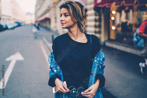 Concept of trendy style street fashion and jeans denim, attractive positive caucasian hipster girl with casual hairstyle and smartphone in hand walking in autumn city and thoughtfully looking aside #814885334