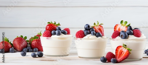 Vanilla dessert cups adorned with a medley of fresh strawberries blueberries and raspberries placed on a white wooden surface for a visually appealing copy space image photo