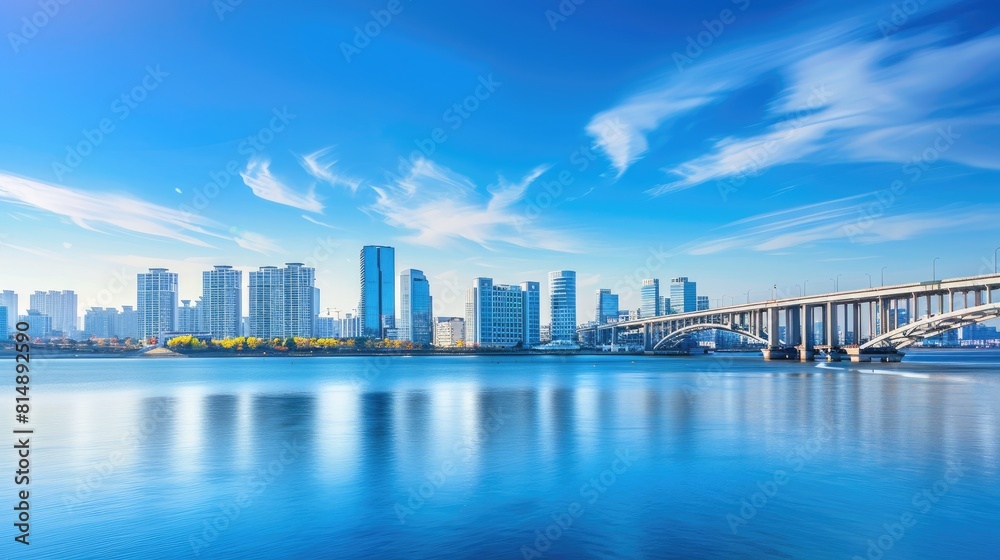 Fototapeta premium the picturesque cityscape and bridge on a sunlit day, where tranquil waters reflect the clear blue sky dotted with wispy clouds.