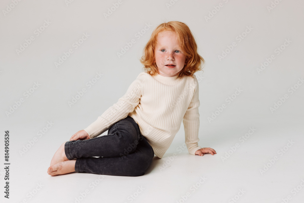 Little girl with red hair sitting in front of white background, innocent beauty and childhood happiness Little girl with red hair sitting in front of white background, innocent beauty and childhood happiness