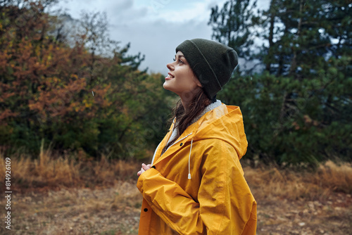 A young woman in a yellow raincoat standing in a serene field surrounded by nature beauty and travel concept
