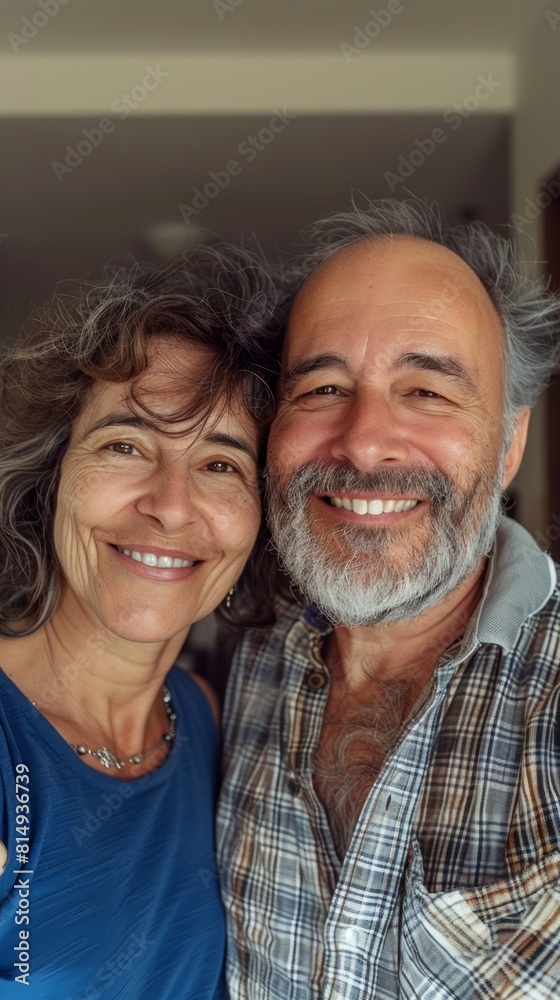 A joyful couple both smiling with the man sporting a gray beard taking a selfie in a room with a blurred background. A joyful couple both smiling with the man sporting a gray beard taking a selfie in a room with a blurred background.