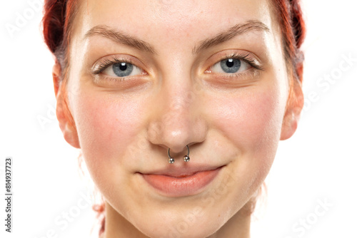 Portrait of a young smiling woman without makeup, nose piercing and blue eyes on a white background