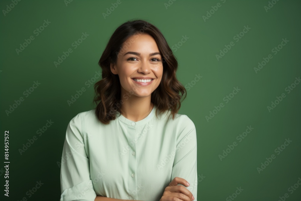 Fototapeta premium Portrait of a grinning woman in her 30s with arms crossed on pastel green background