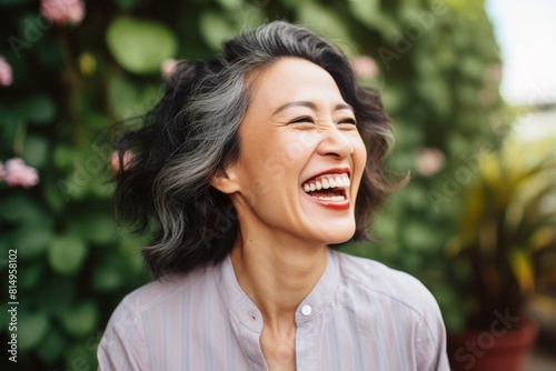 Portrait of a smiling asian woman in her 40s laughing while standing against pastel green background