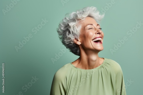 Portrait of a glad woman in her 60s laughing over pastel green background