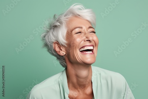 Portrait of a glad woman in her 60s laughing over pastel green background