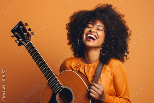 Portrait of a happy afro-american woman in her 30s playing the guitar over pastel orange background