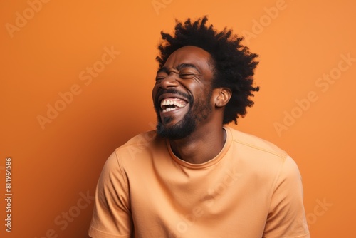 Portrait of a smiling afro-american man in his 30s laughing over pastel orange background