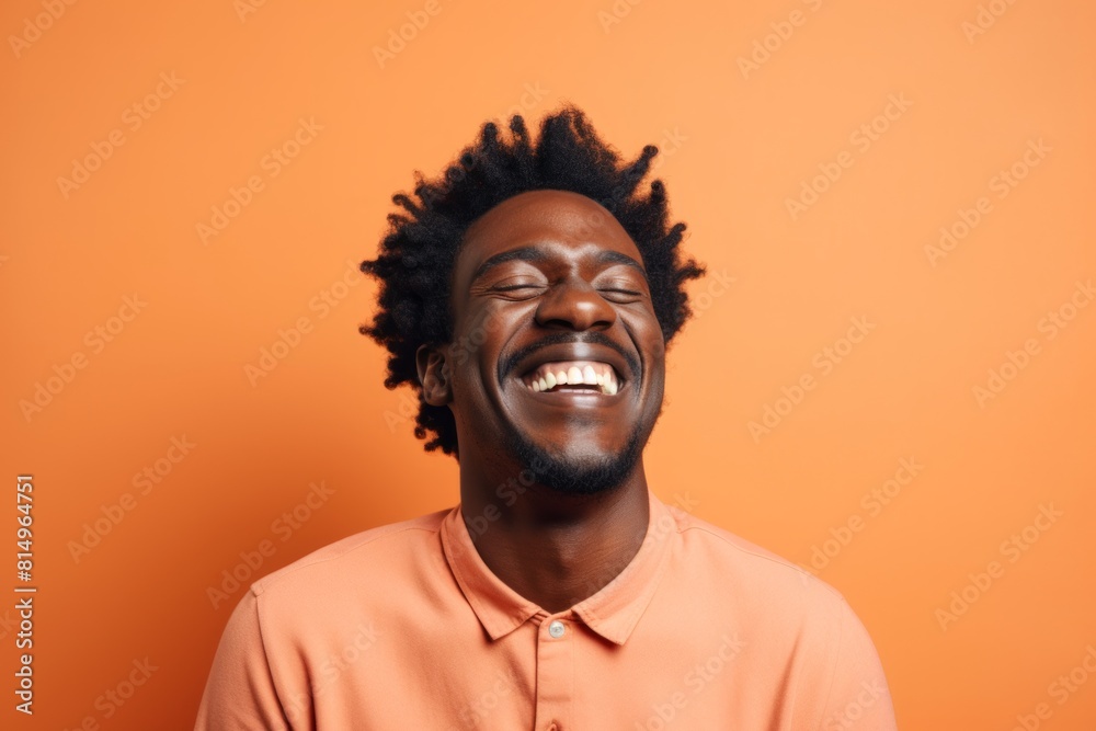 Portrait of a smiling afro-american man in his 30s laughing over pastel orange background Portrait of a smiling afro-american man in his 30s laughing over pastel orange background