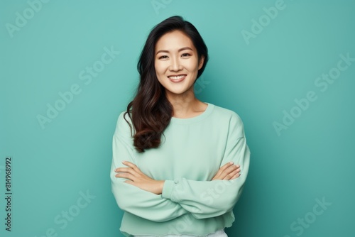 Portrait of a blissful asian woman in her 30s with arms crossed over pastel teal background © Markus Schröder