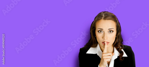 Portrait of young serious business woman keeping finger on her lips and asking to keep quiet, isolated purple violet background. Wide banner image with empty slogan text ad area.