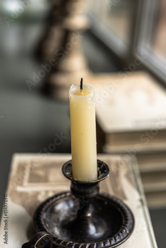 A candle stands on book pile on windowsill, abstract window background. Books and chessman in the defocused background. Intelligence, knowledge concept