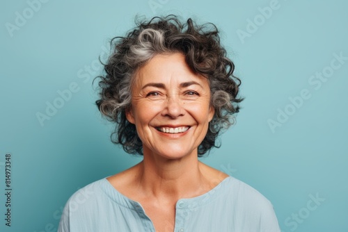 Portrait of a content afro-american woman in her 50s smiling at the camera in front of pastel teal background