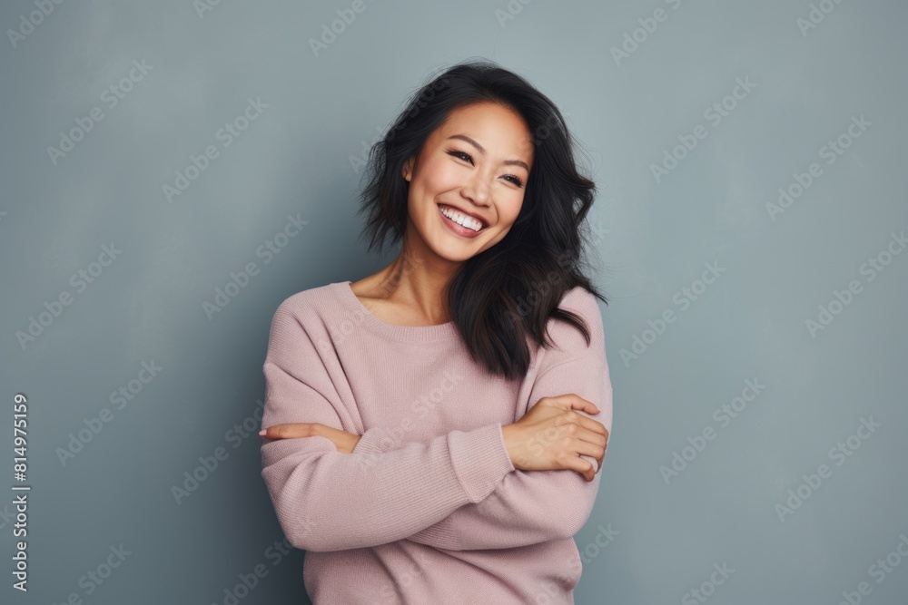 Portrait of a cheerful asian woman in her 30s with arms crossed while standing against pastel gray background Portrait of a cheerful asian woman in her 30s with arms crossed while standing against pastel gray background