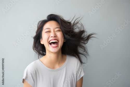 Portrait of a jovial asian woman in her 30s laughing isolated in pastel gray background