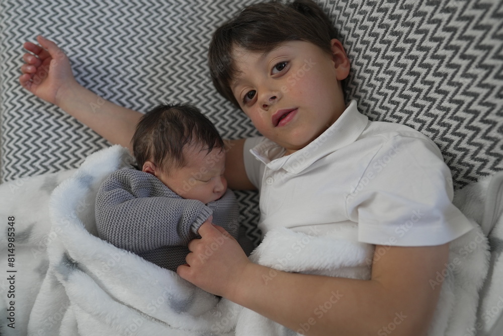 An older brother snuggles close with his newborn sibling, highlighting a sweet and serene moment of bonding and love between brothers. An older brother snuggles close with his newborn sibling, highlighting a sweet and serene moment of bonding and love between brothers.
