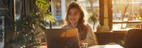 A cheerful young woman enjoys working on her laptop in a sunny café, exemplifying flexible work environments photo