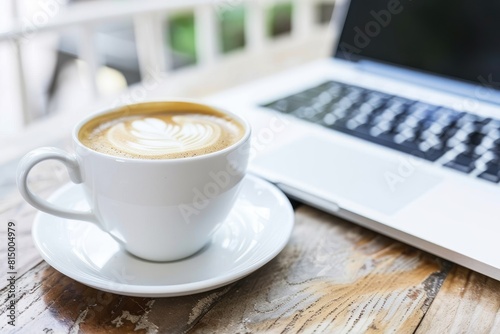 A cup of coffee sits on a saucer next to an open laptop on a table